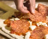 Hand belegt Pizza mit Salami. Frage: darf man in der schwangerschaft salami essen? Die Antwort ist ja, wenn sie gut durchgegart ist.