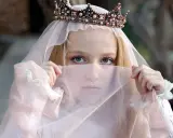Ein Mädchen mit Krone und Schleier, wie eine Prinzessin aus Herr der Ringe Namen weiblich, blickt geheimnisvoll hervor.