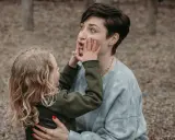 Ein kleines Kind drückt der Mutter spielerisch die Hände ins Gesicht. Vielleicht fragt es sich, warum beleidigen Kinder andere Kinder, wenn sie doch so viel Spaß haben können.
