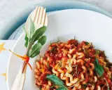 Gedrehte Pasta mit Bolognese-Sauce, garniert mit Salbei. Ein Holzgabel-Set mit Kräutern, passend zur bolognese schwangerschaft.