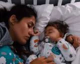 Mutter und Baby schlafen eng aneinander gekuschelt im Bett. Das Baby hat einen Schnuller im Mund. Ein friedlicher Moment, der zeigt, dass man nicht immer alleine ins Bett gehen muss.