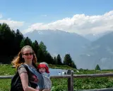 Frau mit Baby im Tragetuch genießt die Berglandschaft. Ein Beispiel für alleine reisen mit Kind.