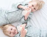 Zwei süße Jungen in karierten Pyjamas trinken aus Fläschchen. Perfekt für Inspiration für Zwillingsnamen Jungen!