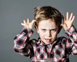 Ein frecher Junge mit Sommersprossen zieht Grimassen und steckt die Zunge heraus, ein Ausdruck dafür, wenn Kinder frech und respektlos sind.