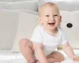 Ein strahlendes Baby, ein echtes Kind der Sonne, sitzt auf einem Bett. Elias' Lachen ist ansteckend.