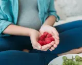 Schwangere Frau hält Himbeeren in den Händen. Die roten Früchte sind ein gesunder Snack während der Schwangerschaft.