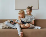 Geschwisterliebe: Ein Mädchen umarmt ihren Bruder, während sie gemeinsam auf dem Sofa lesen. Eine schöne Darstellung ihrer Beziehung.