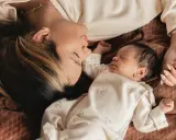 Mutter und Baby liegen eng beieinander. Die Mutter schaut liebevoll auf ihr schlafendes Kind. Ein Moment der Ruhe und Geborgenheit, der die **Baby-Begrenzung beim Schlafen** symbolisiert.