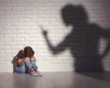 Ein Mädchen kauert weinend auf dem Boden, während ein bedrohlicher Schatten einer erwachsenen Person an der Wand steht. Psychologie: Mutter hasst Tochter?