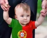 Ein süßes Baby mit portugiesischer Flagge auf dem T-Shirt, gehalten von einer Hand. Vielleicht ein zukünftiger João oder Miguel, inspiriert von portugiesischen Jungennamen.