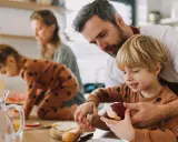 Vater hilft Sohn beim Schälen eines Apfels. Die Familie bereitet gemeinsam das Essen vor, ein Beispiel für geteilten mental load.