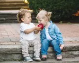 Zwei kleine Freunde teilen sich einen roten Apfel.