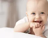Ein lächelndes Baby mit blauen Augen, das auf einer weißen Decke liegt. Vielleicht ein zukünftiger Träger von langen Jungennamen wie Maximilian oder Alexander.