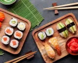 Frischer roher Fisch stillt den Appetit auf Sushi. Nigiri mit Lachs, Maki-Rollen mit Avocado und Garnelen-Sushi auf Holzbrettern.