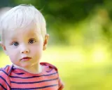 Ein kleiner Junge mit blonden Haaren und blauen Augen blickt neugierig in die Kamera. Sein gestreiftes Shirt erinnert an die Vielfalt von Jungennamen international.