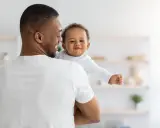 Ein Vater hält sein lächelndes Baby. Vielleicht sucht er nach christlichen Jungennamen für seinen kleinen Schatz.