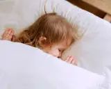 Kleines Kind schläft friedlich im Bett. Ab wann schlafen Kinder alleine ein? Diese süße Szene zeigt einen friedlichen Schlaf.