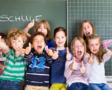 Fröhliche Kinder mit Daumen hoch vor einer Tafel mit dem Wort "SCHULE". Ein perfekter erster schultag!