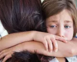 Ein trauriges Kind umarmt seine Mutter. In der Grundschule darf das Kind nicht mitspielen, es fühlt sich ausgeschlossen.