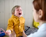 Ein weinendes Kind im Kindergarten, das nach Mama ruft. Die Erzieherin versucht, das kleine Mädchen zu trösten.