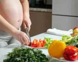 Schwangere bereitet gesunde Mahlzeit zu. Bunte Paprika, Tomaten und frisches Gemüse für eine gute Ernährung während der Schwangerschaft.