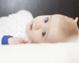 Ein Baby mit strahlend blauen Augen und blonden Haaren, das neugierig in die Kamera blickt. Ein süßer kleiner Kerl, der bestimmt mal einer der freche jungennamen tragen wird.