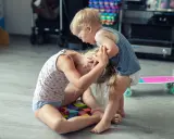 Ein aggressives Kind hält das Haar eines anderen Kindes, das auf bunten Holzklötzen sitzt.