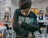 Ein Junge hält ein Buch, während andere Kinder im Hintergrund spielen. Er wirkt traurig, als ob mein Kind im Kindergarten ausgeschlossen wird.