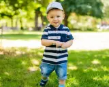 Ein lächelnder Junge mit Kappe und gestreiftem Polo-Shirt im Park. Vielleicht heißt er Finn, Leo oder Noah – beliebte Jungennamen mit 4 Buchstaben.
