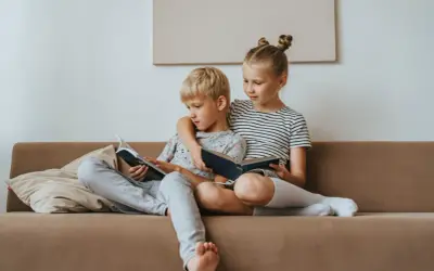 Geschwisterliebe: Ein Mädchen umarmt ihren Bruder, während sie gemeinsam auf dem Sofa lesen. Eine schöne Darstellung ihrer Beziehung.
