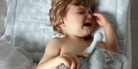 Ein weinendes Kind, 1 Jahr alt, in der Trotzphase, hält seinen Kuschelhasen.