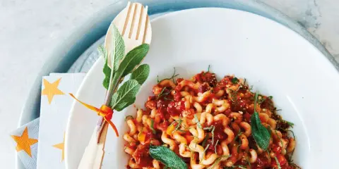 Gedrehte Pasta mit Bolognese-Sauce, garniert mit Salbei. Ein Holzgabel-Set mit Kräutern, passend zur bolognese schwangerschaft.