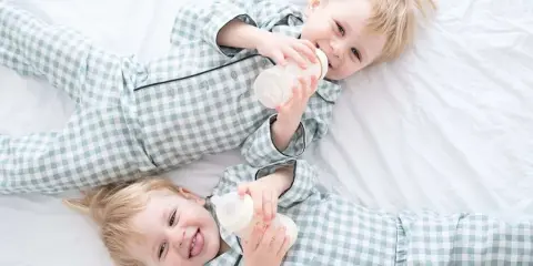 Zwei süße Jungen in karierten Pyjamas trinken aus Fläschchen. Perfekt für Inspiration für Zwillingsnamen Jungen!