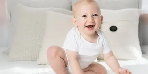 Ein strahlendes Baby, ein echtes Kind der Sonne, sitzt auf einem Bett. Elias' Lachen ist ansteckend.