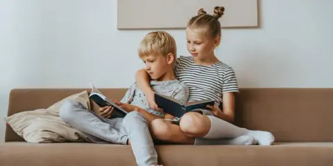 Geschwisterliebe: Ein Mädchen umarmt ihren Bruder, während sie gemeinsam auf dem Sofa lesen. Eine schöne Darstellung ihrer Beziehung.