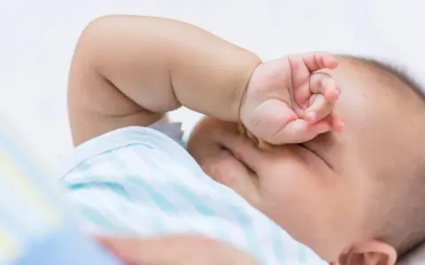 Baby im REM-Schlaf, die Hand vor den Augen, träumt süß.