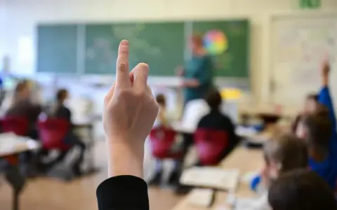 Ein Schüler hebt die Hand, um eine Frage zu stellen. Wie lange muss man in die Schule gehen? Die Antwort liegt im Unterricht.