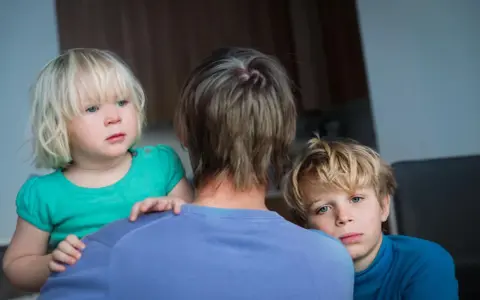 Zwei Kinder blicken besorgt über die Schulter einer Person. Die **Trennung wegen unterschiedlicher Erziehung** scheint sie zu belasten.