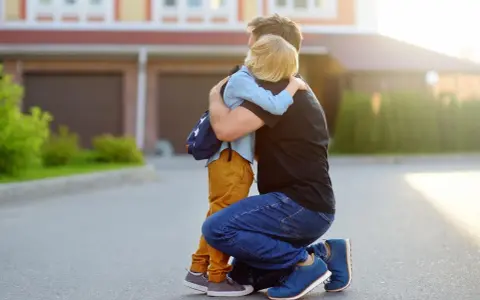 Vater umarmt seinen Sohn mit Rucksack. Ein guter Schulstart nach den Ferien beginnt mit einer liebevollen Umarmung.