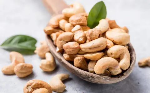 Holzkelle voller Cashewkerne, ideal für die Schwangerschaft. Zwei grüne Blätter liegen daneben.
