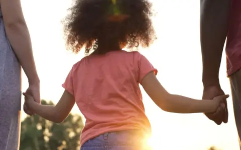Kind hält Hände von Eltern. Die gesetzliche Regelung Kinderbetreuung Trennung soll das Wohl des Kindes sichern.