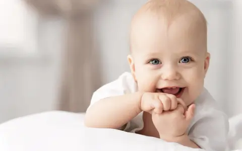 Ein lächelndes Baby mit blauen Augen, das auf einer weißen Decke liegt. Vielleicht ein zukünftiger Max oder Mika, einer der beliebten Jungennamen mit M.