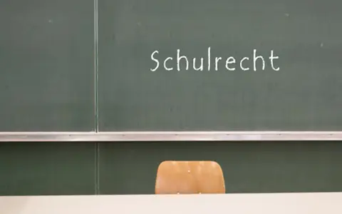 Grüne Tafel mit der Aufschrift "Schulrecht". Ein leerer Stuhl davor. Hier werden die Elternpflichten für Hausaufgaben und das Schulrecht thematisiert.