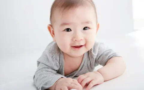 Lächelndes Baby in grauem Shirt auf weißem Hintergrund.