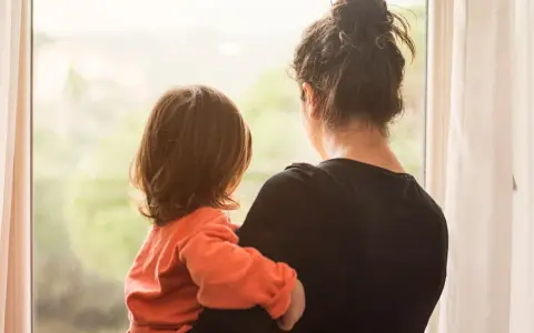 Ein Kind kuschelt sich an seine Mutter, die aus dem Fenster schaut. Die Szene erweckt Gefühle von Geborgenheit, aber auch die leise Angst, die Mutter zu verlieren.