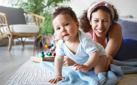 Ein Baby krabbelt neugierig, seine Mutter lächelt. Ein starker Wille zeigt sich schon früh, die Bedeutung des Namens wird gelebt.