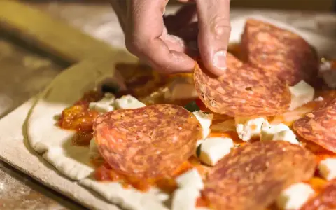 Hand belegt Pizza mit Salami. Frage: darf man in der schwangerschaft salami essen? Die Antwort ist ja, wenn sie gut durchgegart ist.