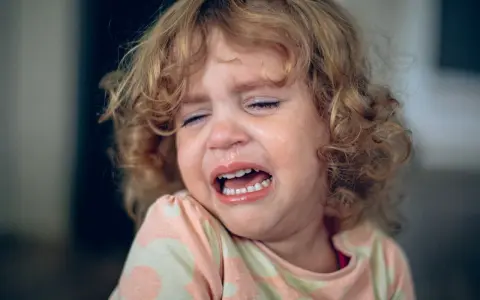 Ein kleines Mädchen mit lockigen Haaren weint bitterlich. Tränen laufen über ihr Gesicht, die Augen sind geschlossen. Ein Ausdruck von starkem **Wut bei Kindern** ist deutlich zu sehen.