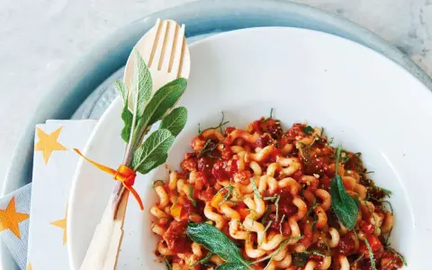 Gedrehte Pasta mit Bolognese-Sauce, garniert mit Salbei. Ein Holzgabel-Set mit Kräutern, passend zur bolognese schwangerschaft.