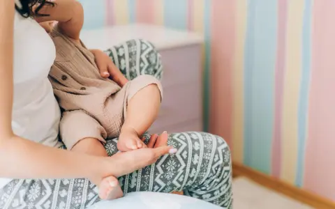 Mutter hält ihr Baby, das auf ihrem Schoß sitzt. Die Streifenwand im Hintergrund ist farbenfroh. Wenn die Mutter während der Stillzeit Durchfall hat, ist das Baby sicher.